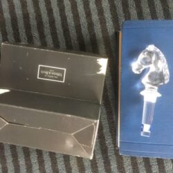 A clear glass bottle stopper and its box on a striped surface.